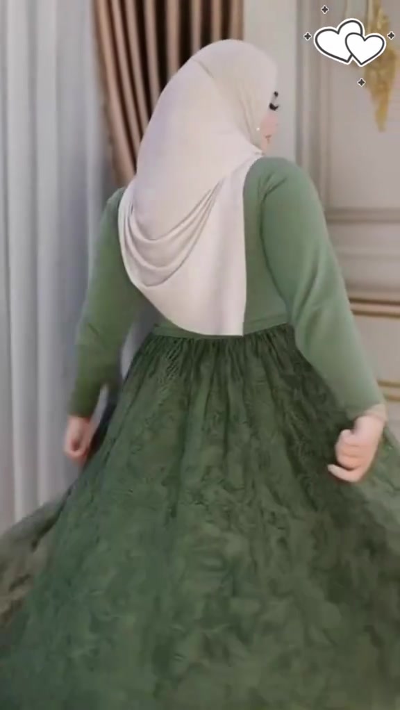 Tampak belakang perempuan berhijab memakai atasan knit hijau sage dan rok maxi brukat hijau yang sedang berputar