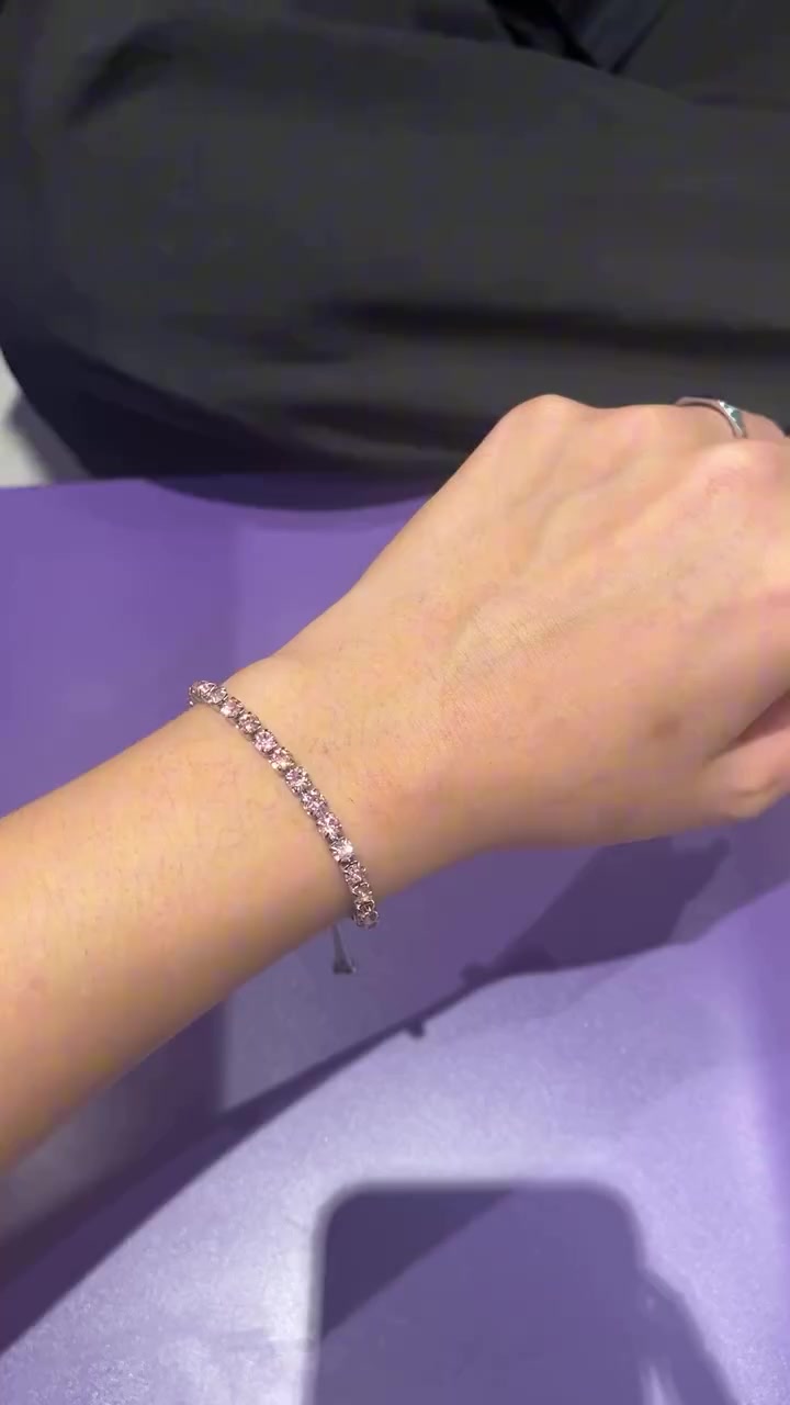 Tennis bracelet batu pink dipakai di pergelangan tangan dengan latar meja ungu
