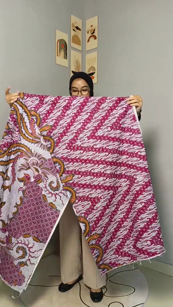Perempuan membentangkan kain batik motif parang warna merah muda fuchsia di depan badannya