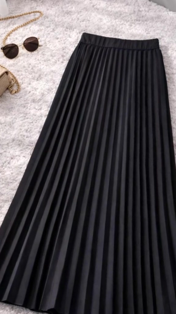 Rok plisket hitam panjang difoto flat lay di karpet berbulu dengan kacamata hitam dan tas rantai di sudut frame