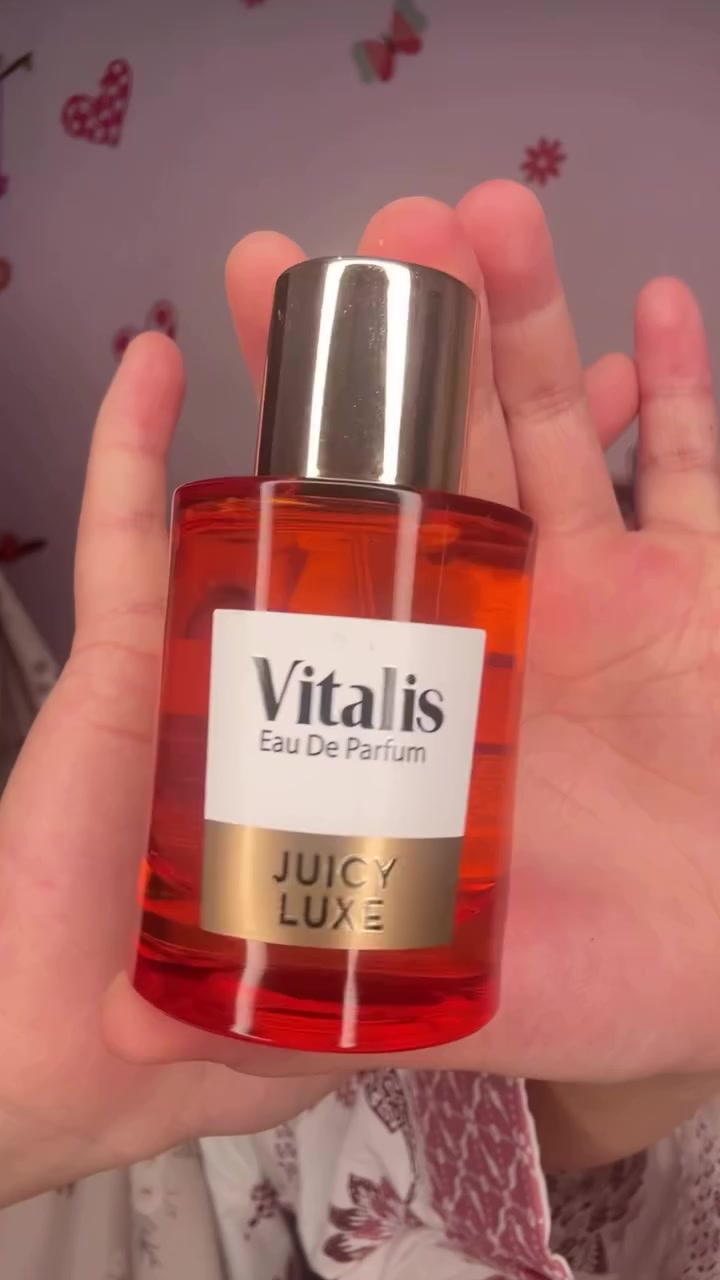 Botol Vitalis EDP Juicy Luxe berisi cairan oranye dipegang di telapak tangan terbuka