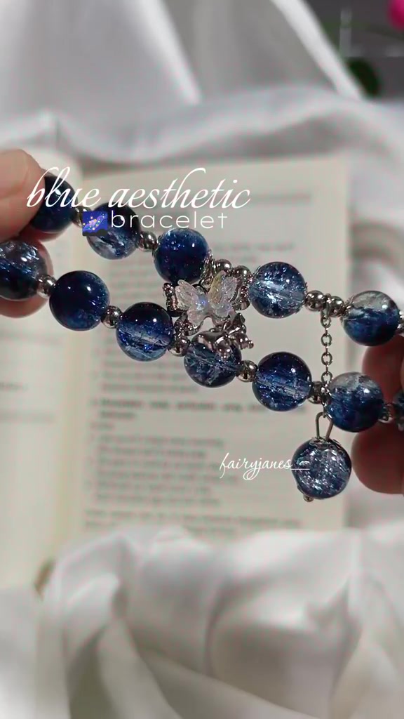 Gelang manik kaca biru dengan efek crackle dan charm kupu-kupu dipegang dengan dua jari