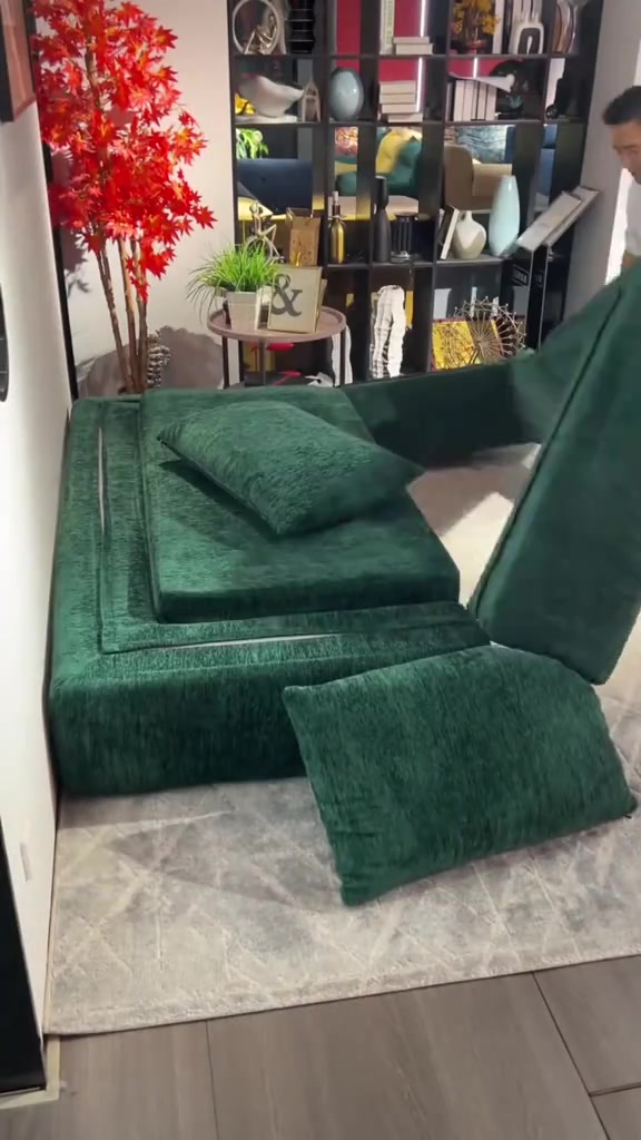 Sofa bed modular hijau tua sedang dibentangkan menjadi tempat tidur di atas karpet terang dengan bantal senada