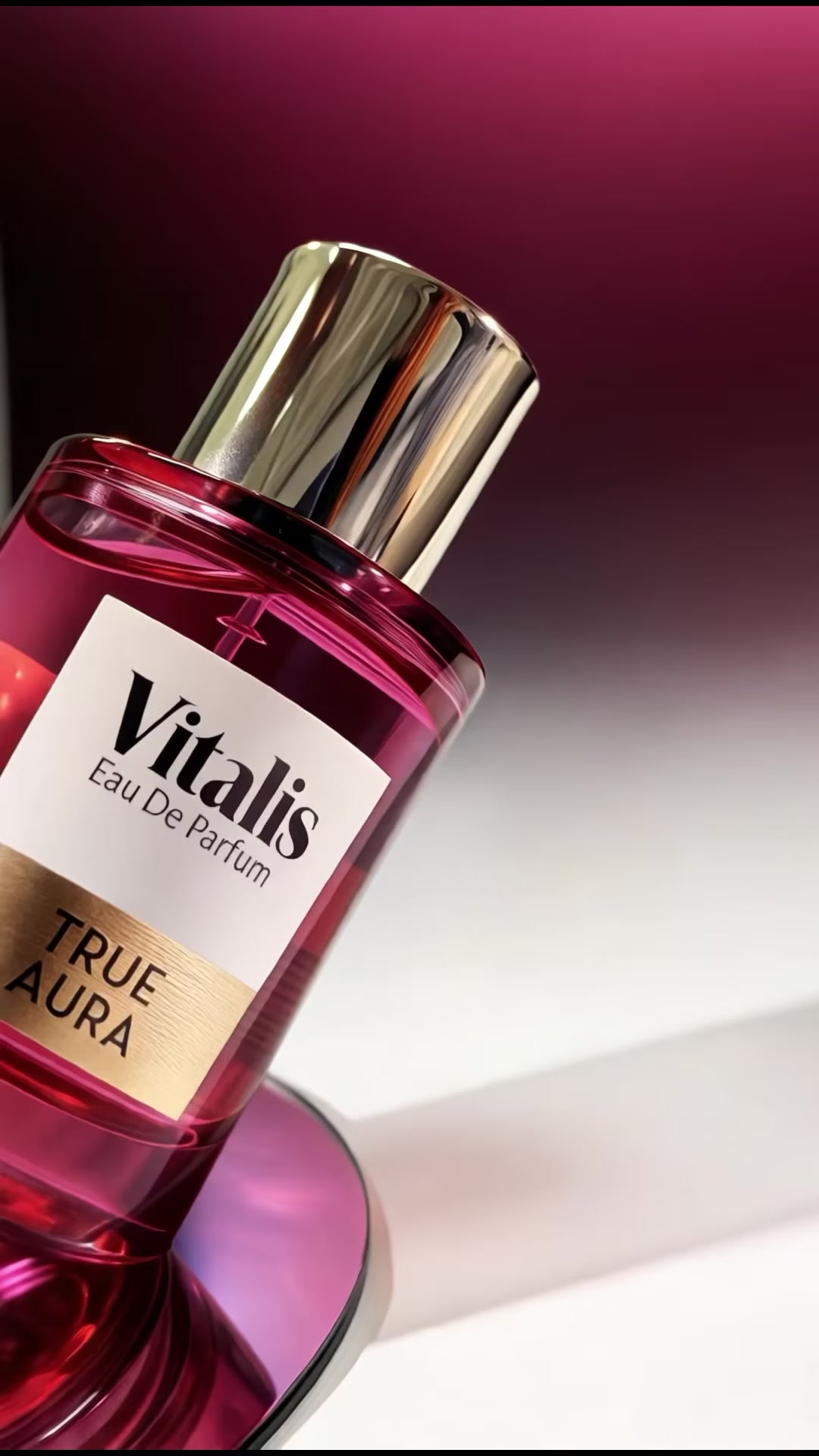 Close up botol Vitalis EDP True Aura berwarna magenta dengan tutup emas di atas pedestal reflektif