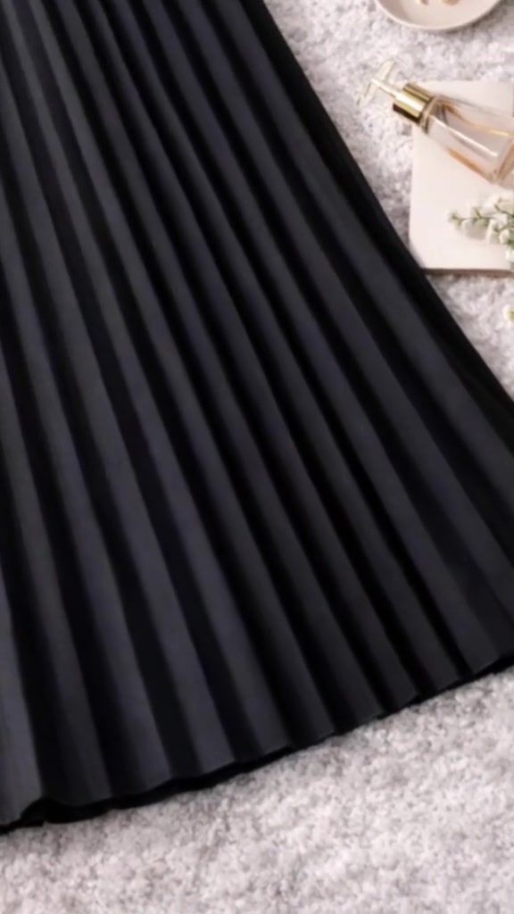 Detail lipatan dan tepi bawah rok plisket hitam yang terbentang di karpet berbulu putih