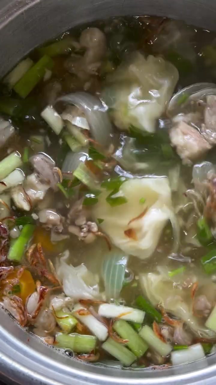 Panci sop tetelan berisi kol, daun bawang, seledri, dan bawang goreng di atas kuah bening yang sedang dimasak