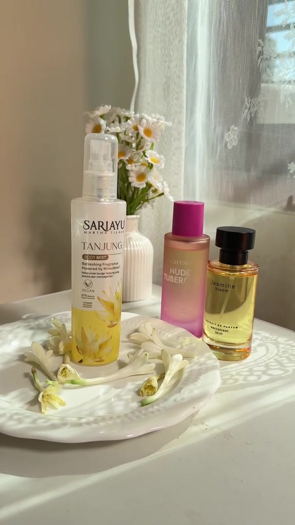 Botol Sariayu Tanjung Body Mist, Careso Nude Tuberose, dan Aerostreet Jasmine Bloom berdiri di piring putih dengan bunga sedap malam dan vas daisi