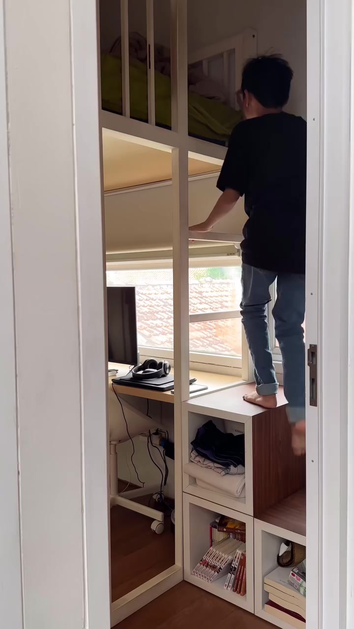 Anak menaiki tangga kubus penyimpanan menuju dipan loft bed putih sementara kolongnya dipakai sebagai meja belajar dan rak buku