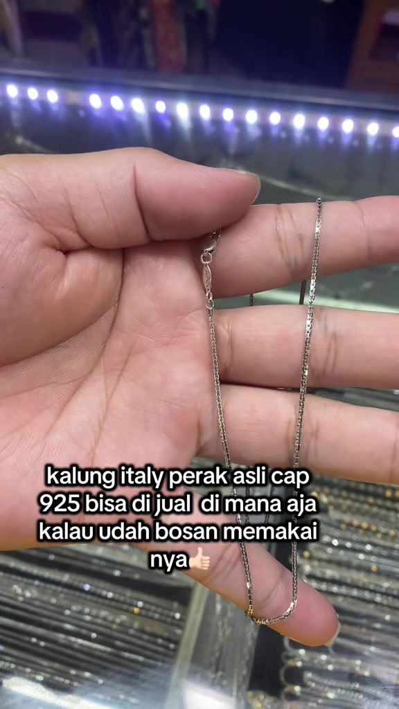 Rantai kalung perak tipis di telapak tangan dengan pengait dan pelat kecil tempat cap 925
