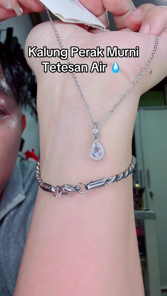 Liontin perak bentuk tetesan air dan gelang rantai perak melingkar di pergelangan tangan