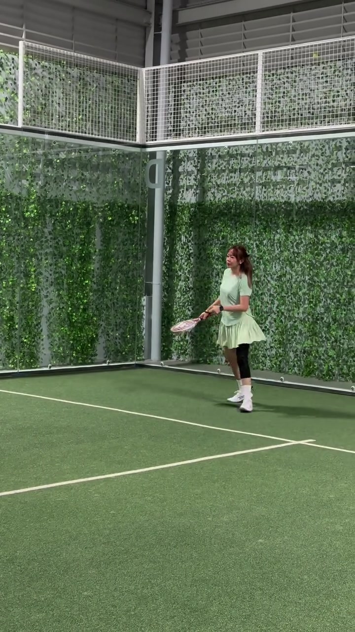 Pemain menunggu bola di lapangan padel berdinding kaca dengan tanaman rambat
