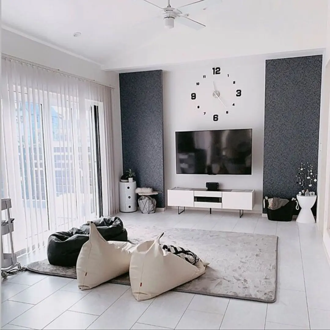 Ruang keluarga serba putih dengan beanbag di atas karpet abu-abu lebar dan meja TV putih rendah di bawah TV yang menempel di dinding