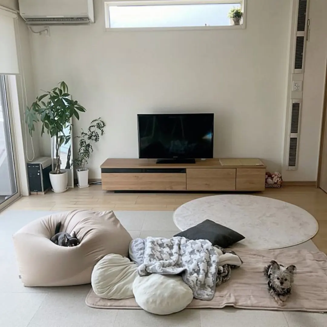 Ruang TV bernuansa Jepang dengan matras lantai krem, karpet bulat, beanbag, dan meja TV kayu rendah