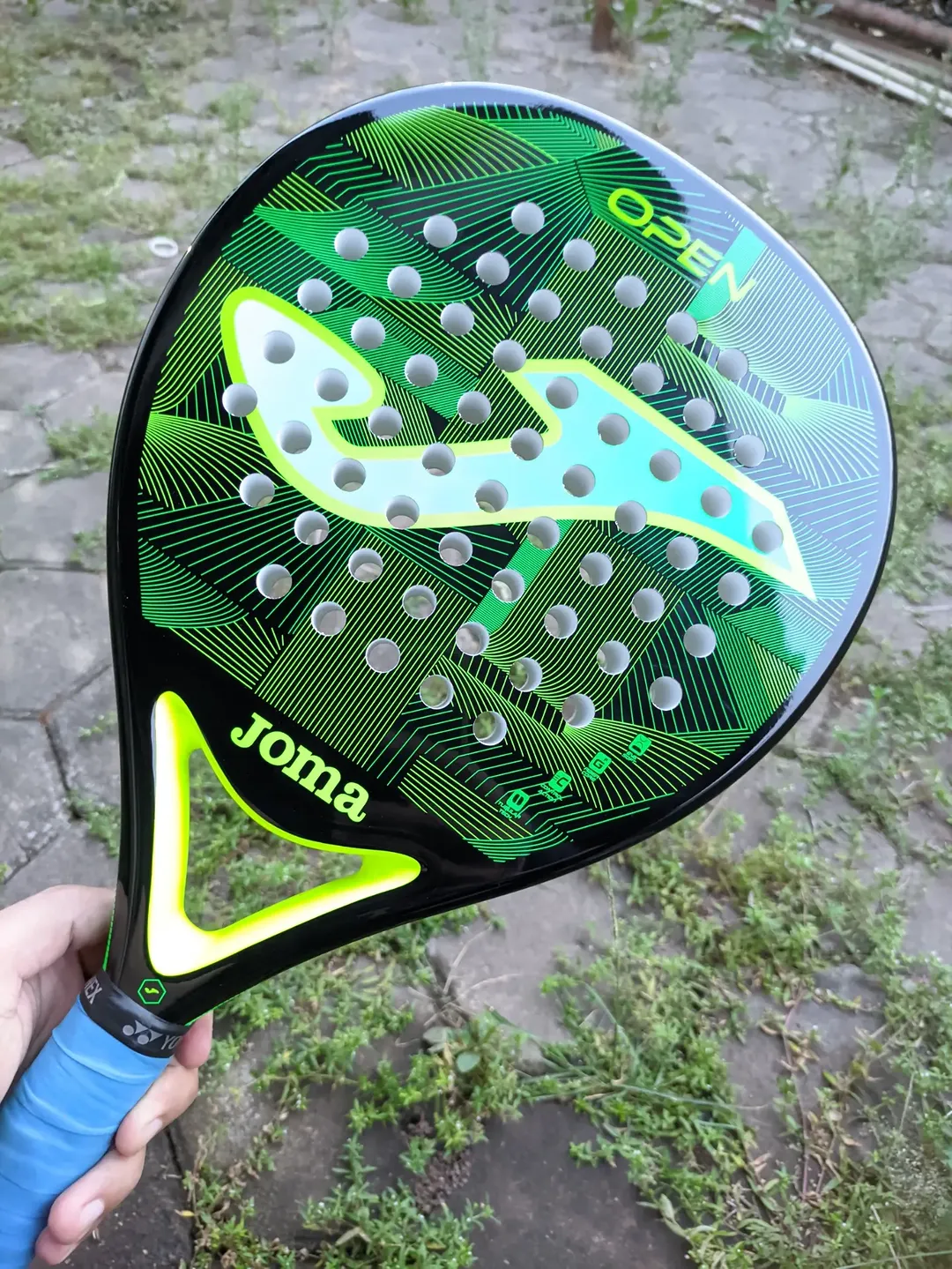 Close-up permukaan raket padel bentuk round berlubang dengan grip overgrip biru