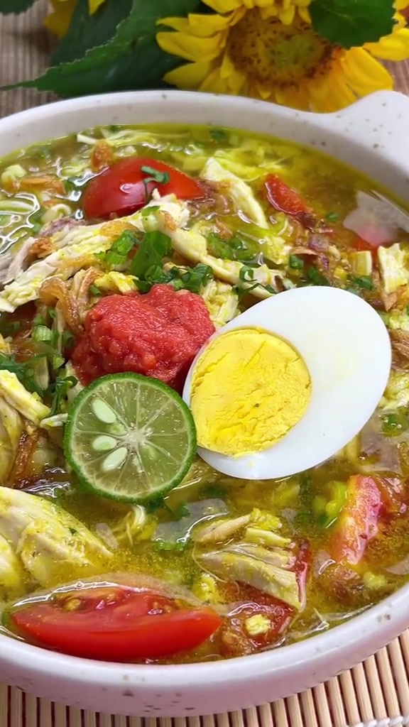 Mangkuk soto ayam lengkap dengan telur rebus, irisan tomat, jeruk nipis, dan sambal