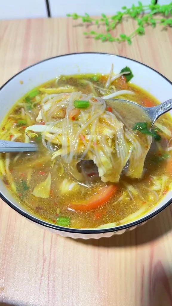 Mangkuk soto ayam dengan sendok mengangkat bihun dari kuah kuning