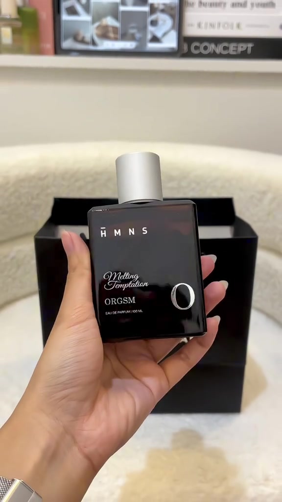Tangan memegang botol HMNS ORGSM Melting Temptation berwarna gelap di depan paper bag hitam HMNS