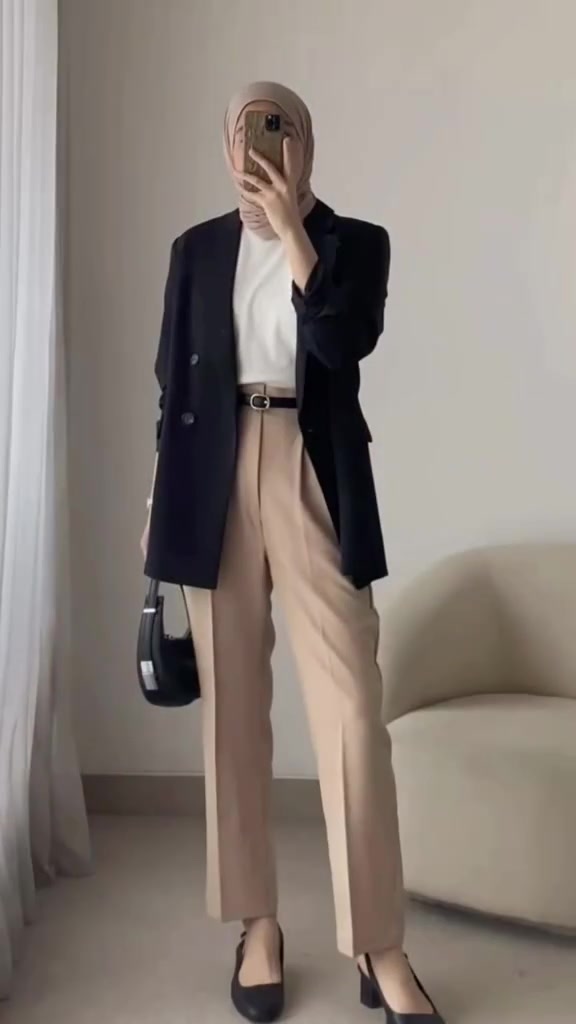 Selfie cermin dengan wajah tertutup ponsel: blazer hitam panjang, atasan putih, celana bahan beige dengan belt hitam, tas hitam kecil, dan heels hitam