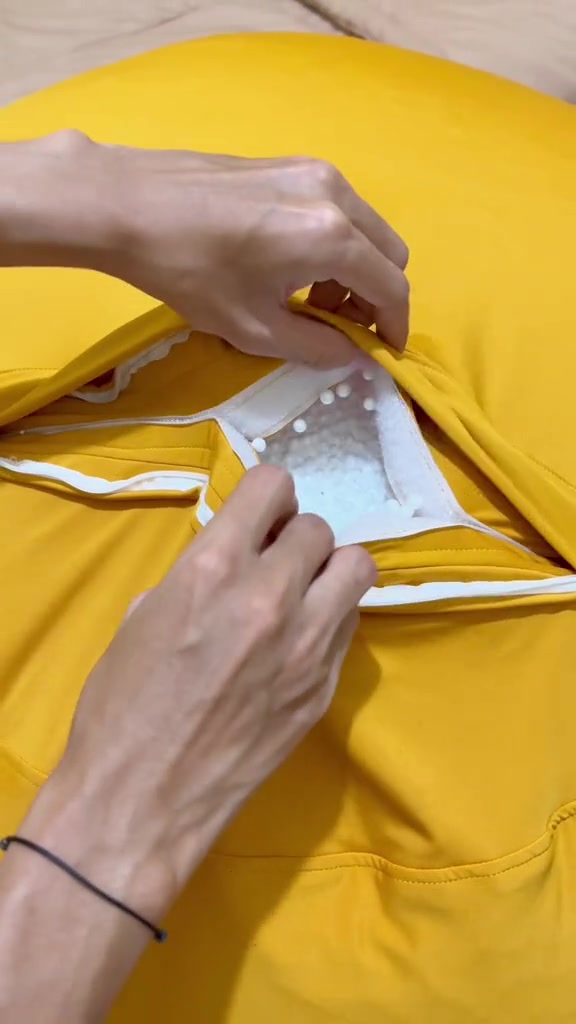 Tangan membuka resleting cover beanbag kuning sampai terlihat butiran styrofoam putih di dalamnya