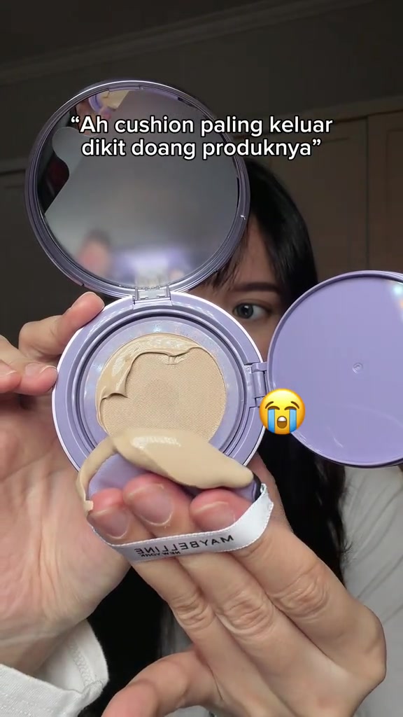 Kompak cushion terbuka dengan produk foundation keluar cukup banyak di atas mesh, puff bertali putih dipegang di depannya