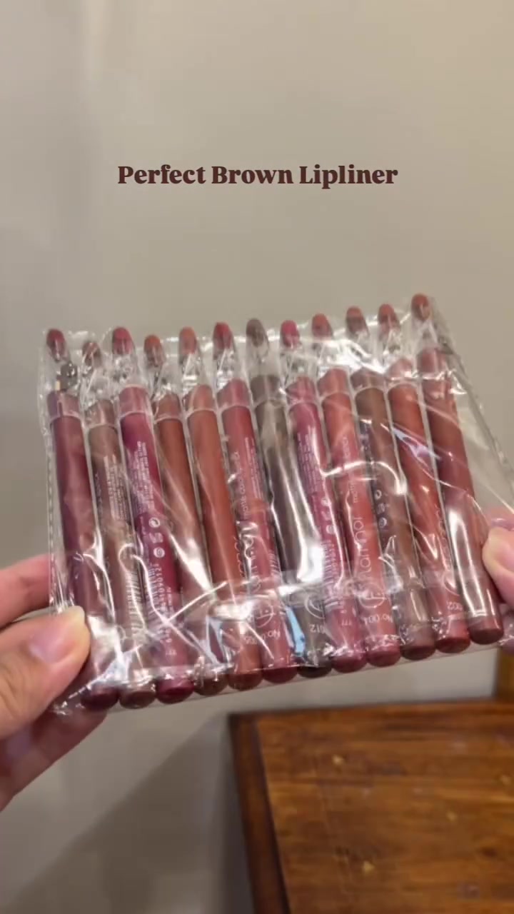 Dua tangan memegang kemasan plastik berisi selusin pensil lip liner warna cokelat