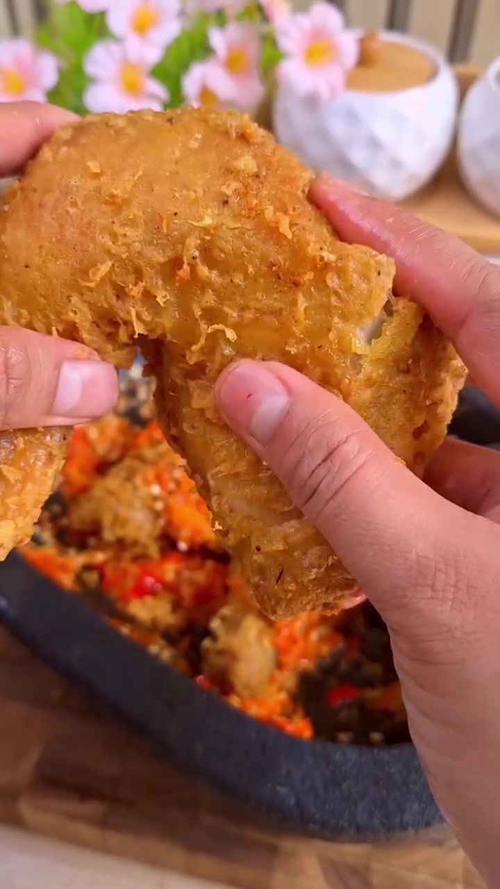 Ayam goreng marinasi berkulit kriuk yang dipegang di atas cobek sambal