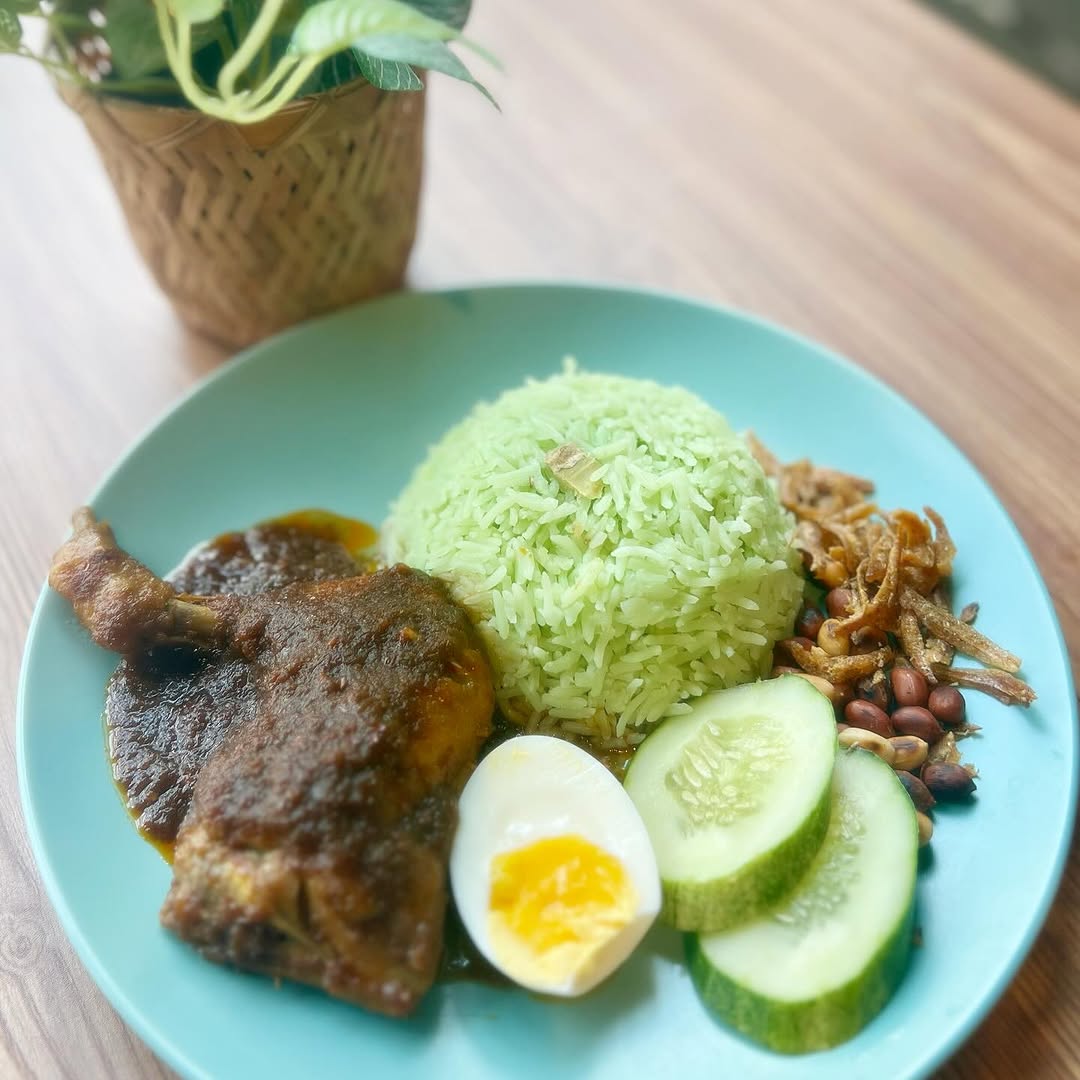 Sepiring nasi lemak pandan dengan ayam goreng sambal, telur rebus, timun, kacang, dan ikan bilis