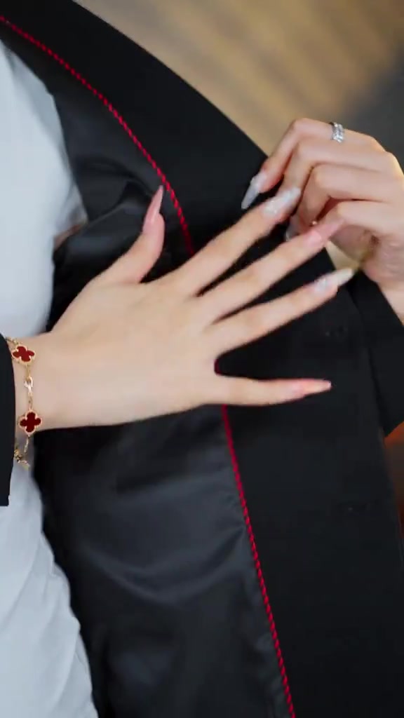 Tangan membuka bagian dalam blazer hitam, memperlihatkan furing satin mengkilap dengan piping merah
