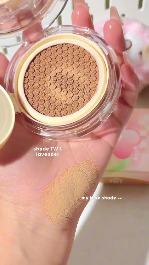 Kompak cushion terbuka memperlihatkan mesh berpola sarang lebah, di sampingnya swatch tipis foundation di telapak tangan