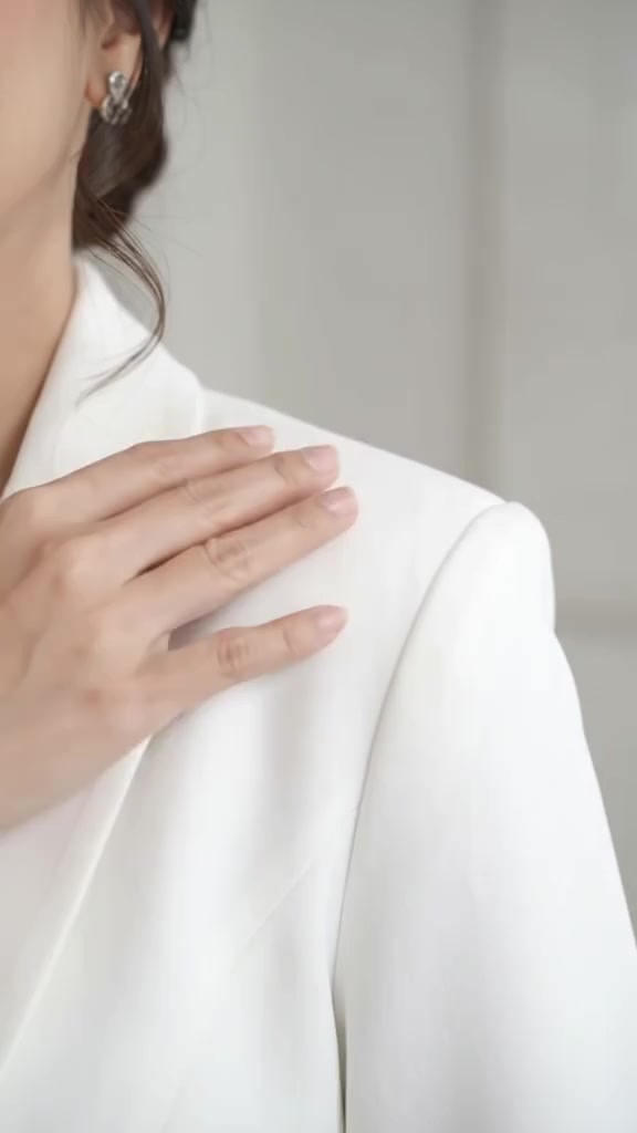 Tangan menyentuh garis bahu blazer putih dari samping dekat, menunjukkan busa bahu dan jahitan kerah