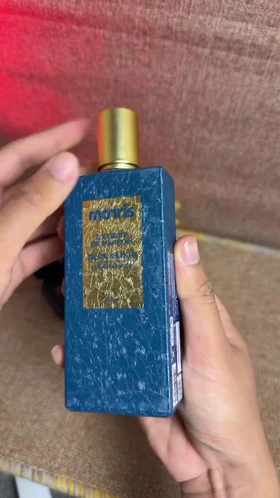 Botol Morris Legacy Edition Blue Elixir berwarna biru bertekstur dengan tutup emas dipegang di atas kain abu-abu