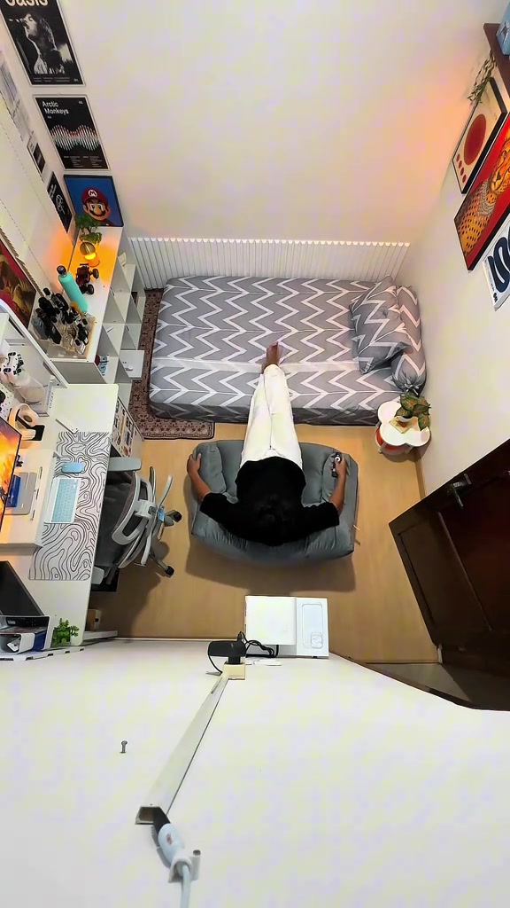 Tampak atas kamar sempit berisi dipan, meja kerja, dan beanbag abu-abu yang dipakai seseorang bersandar