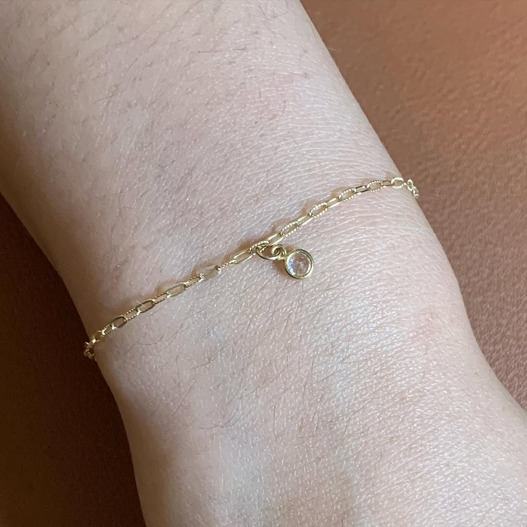 Gelang rantai emas halus dengan satu charm batu bulat di pergelangan tangan