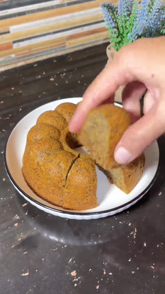 Bolu pisang kukus berbentuk bundt di piring putih dengan satu potong terangkat