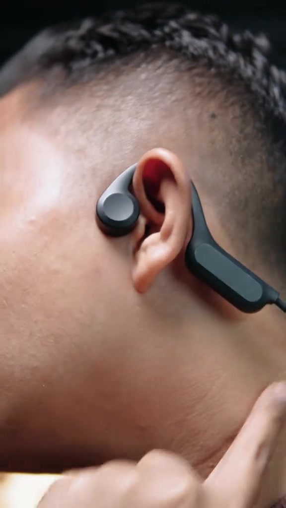 Close-up headset bone conduction hitam dengan bantalan transducer menempel di tulang pipi depan telinga