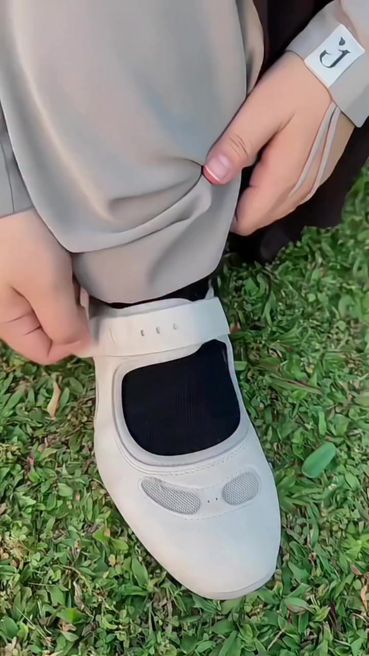 Mary jane sneakers warna beige dengan kaos kaki hitam dipakai berdiri di rumput sambil menyesuaikan strap