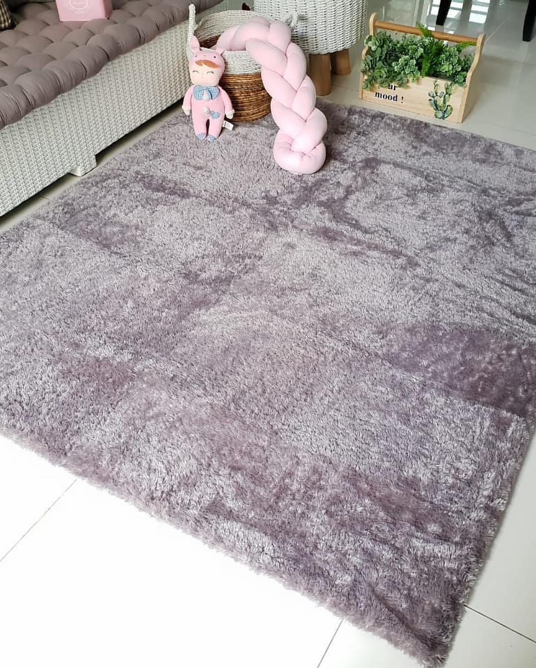 Tekstur karpet bulu abu-abu dengan bantal anyaman bentuk kepang berwarna pink di sudut ruangan