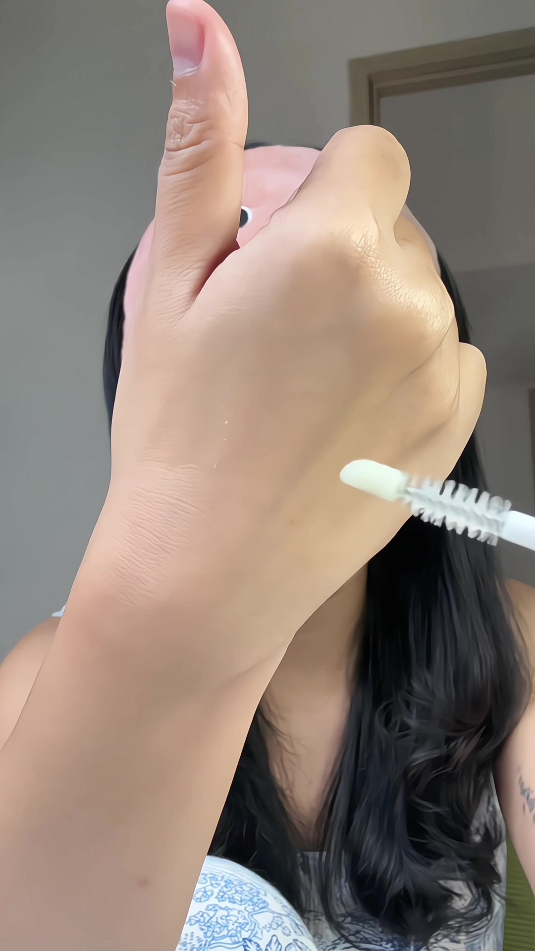 Aplikator spoolie serum bulu mata dengan setetes serum bening di atas punggung tangan