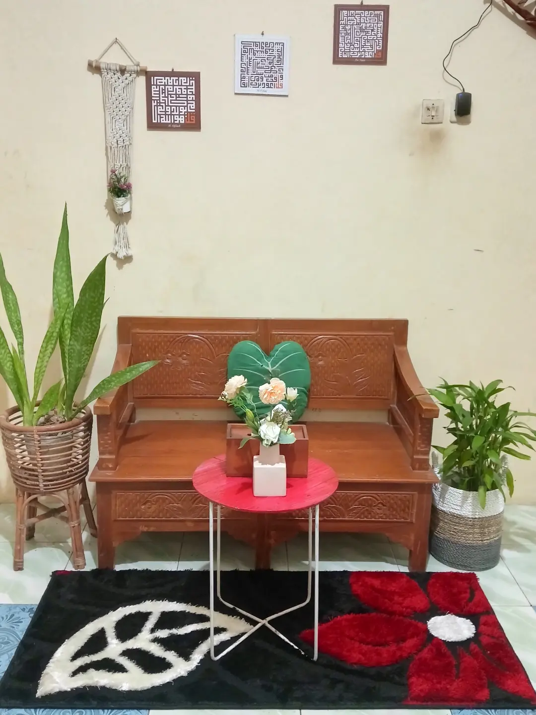 Ruang tamu sederhana dengan bangku kayu ukir dan karpet bulu motif bunga merah hitam