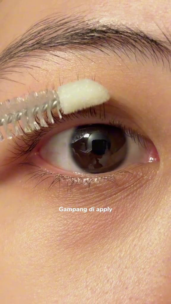 Close-up mata saat aplikator spoolie mengoleskan serum ke garis bulu mata atas