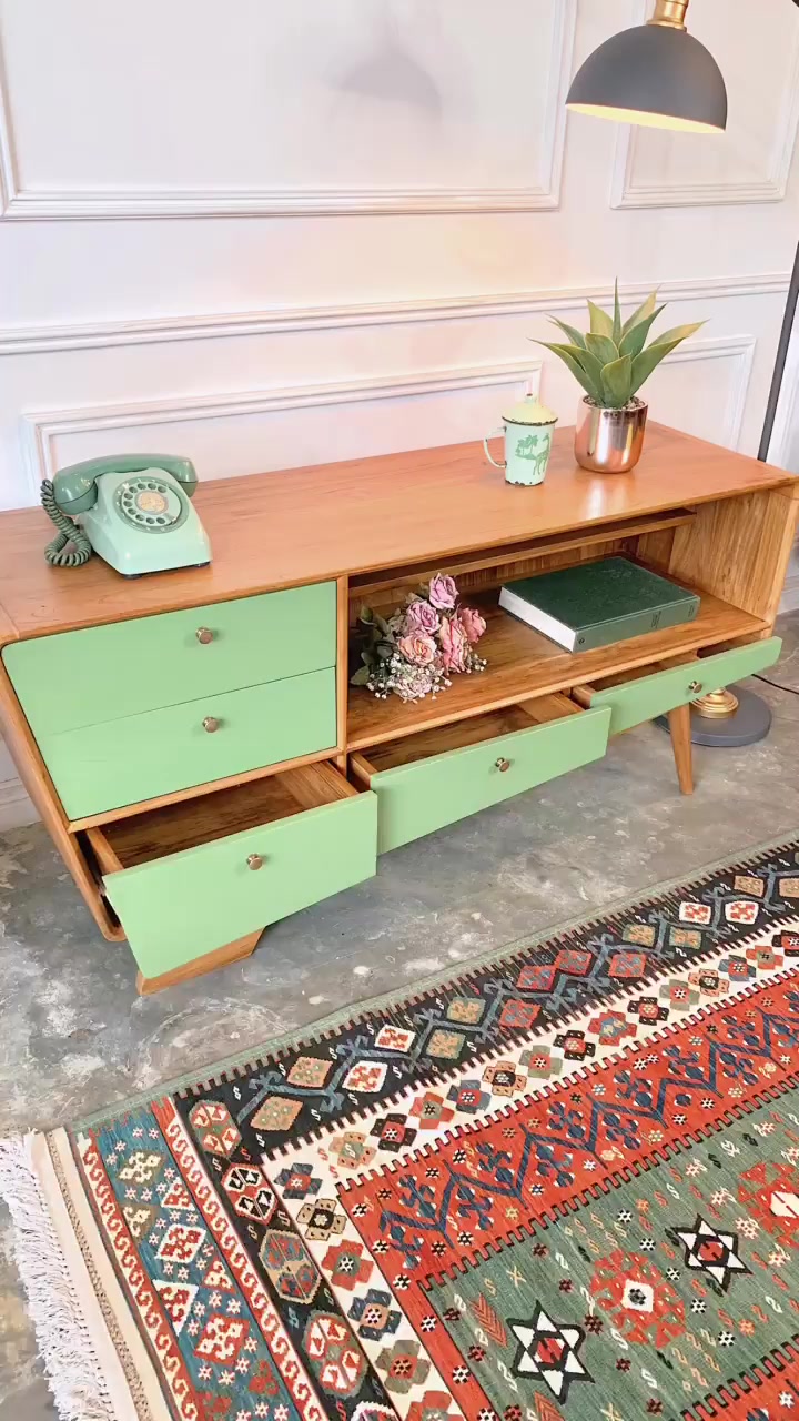 Credenza kayu dengan laci hijau mint yang terbuka, dihias telepon retro dan tanaman di atas karpet bermotif