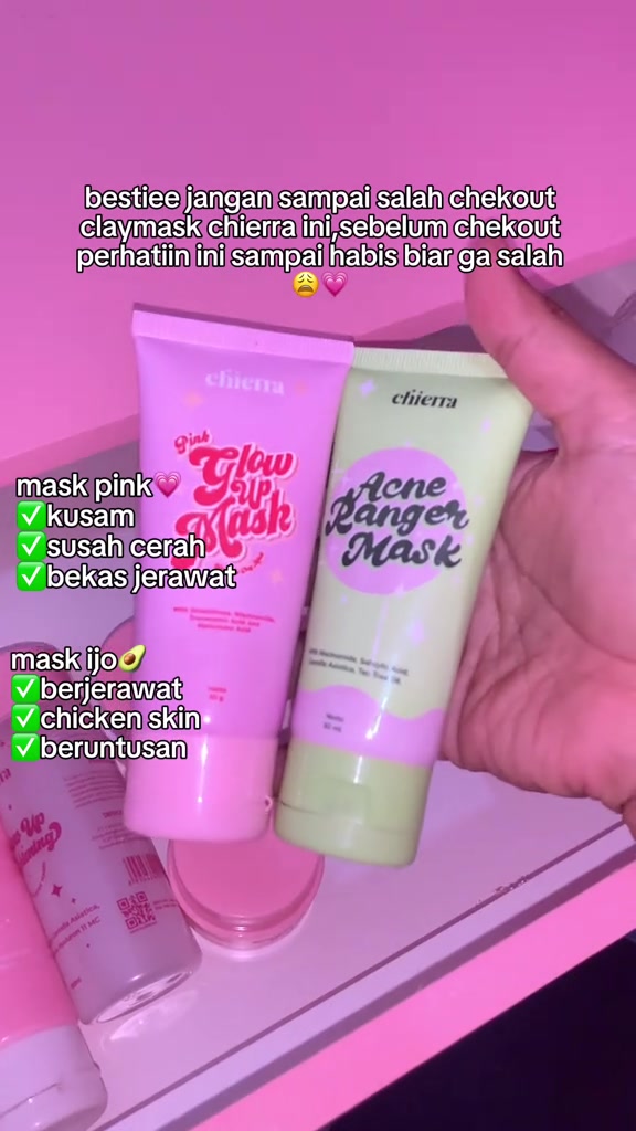 Dua tube clay mask Chierra warna pink dan hijau dipegang satu tangan di atas latar pink