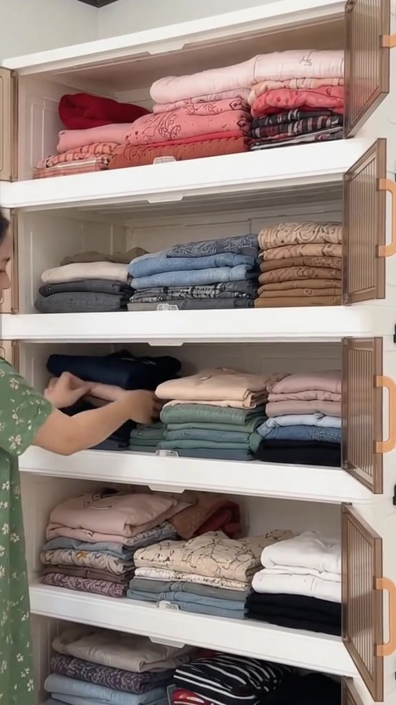 Tangan menata tumpukan baju lipat di rak lemari susun berwarna putih