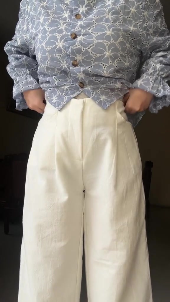 Celana linen putih dengan blouse bermotif biru yang dimasukkan rapi ke dalam pinggang, kedua tangan masuk ke kantong celana