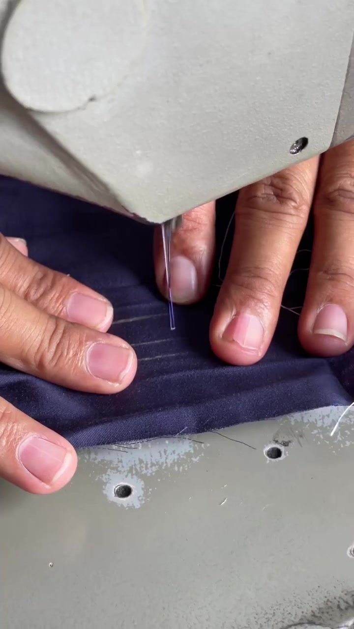 Close-up tangan menjahit kain satin gelap dengan mesin jahit