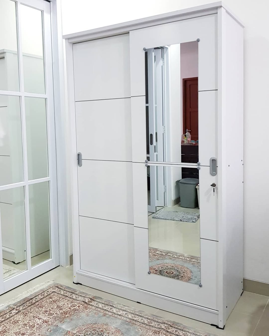 Lemari pakaian pintu sliding putih dengan pintu cermin dilihat dari sudut ruangan berkarpet