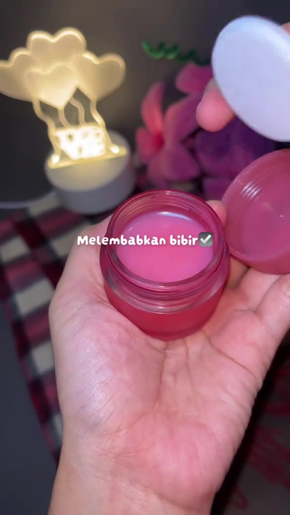 Stoples lip sleeping mask terbuka dengan tekstur balm merah muda di atas telapak tangan