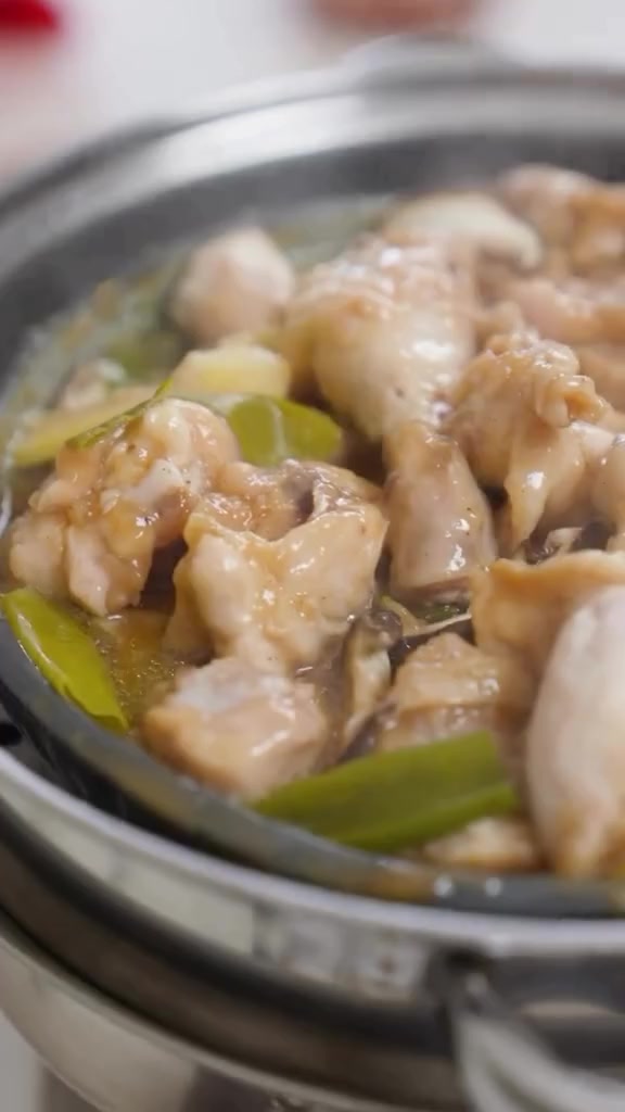 Potongan ayam kukus jahe mengilap di dalam tray kukusan stainless bersama irisan jahe dan batang daun bawang