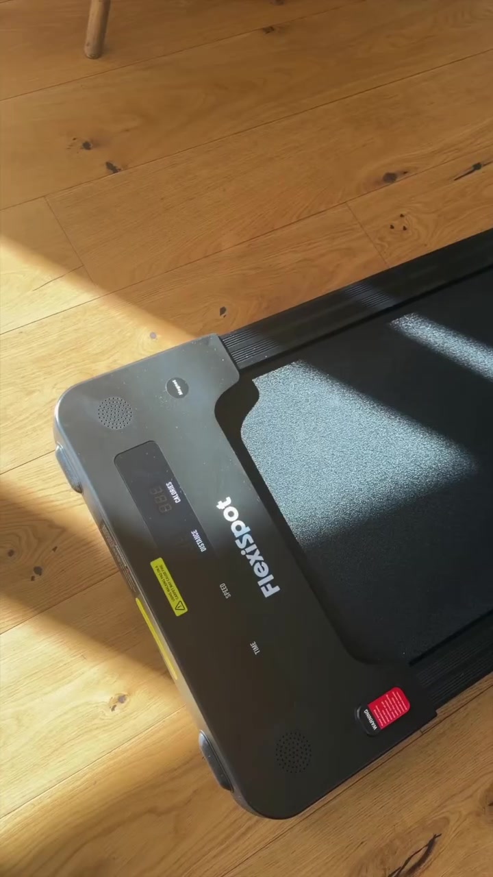 Close-up panel depan walking pad hitam dengan layar kecepatan di lantai kayu