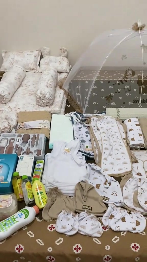 Popok bayi, pakaian, dan beberapa perlengkapan perawatan ditata bersama di atas alas bermotif
